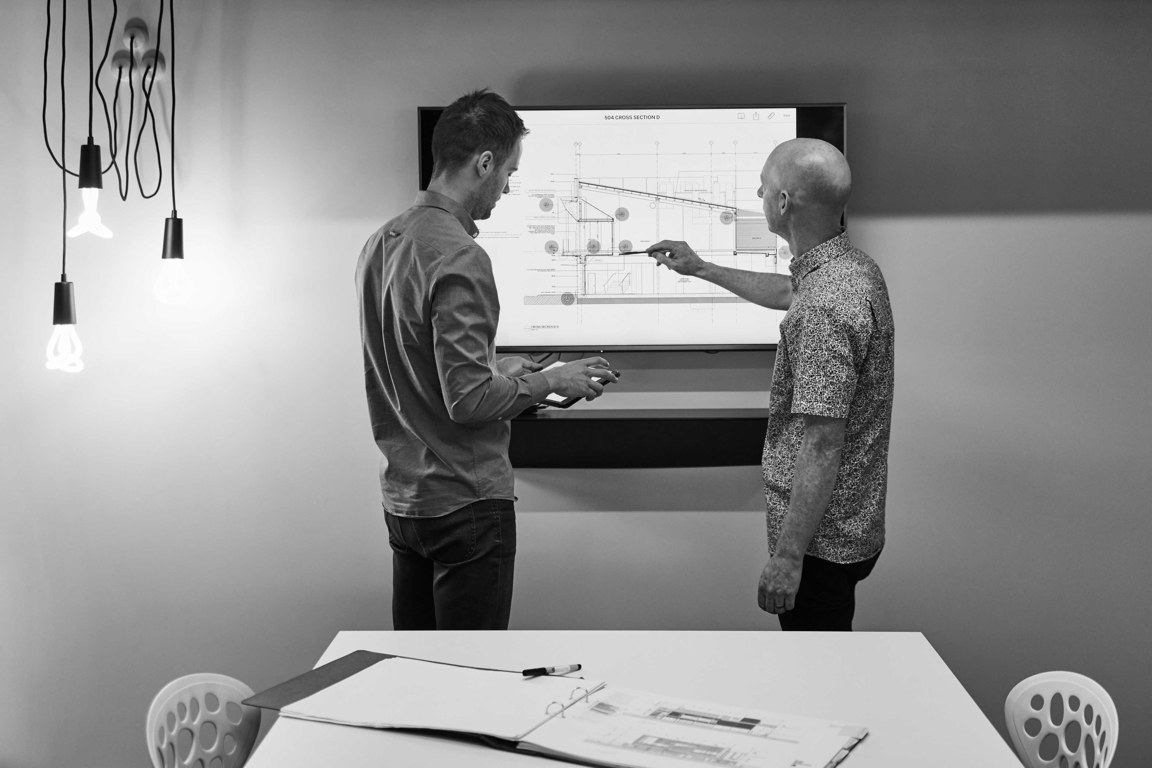 Dean and Nick engaged in work at a wall-mounted digital display