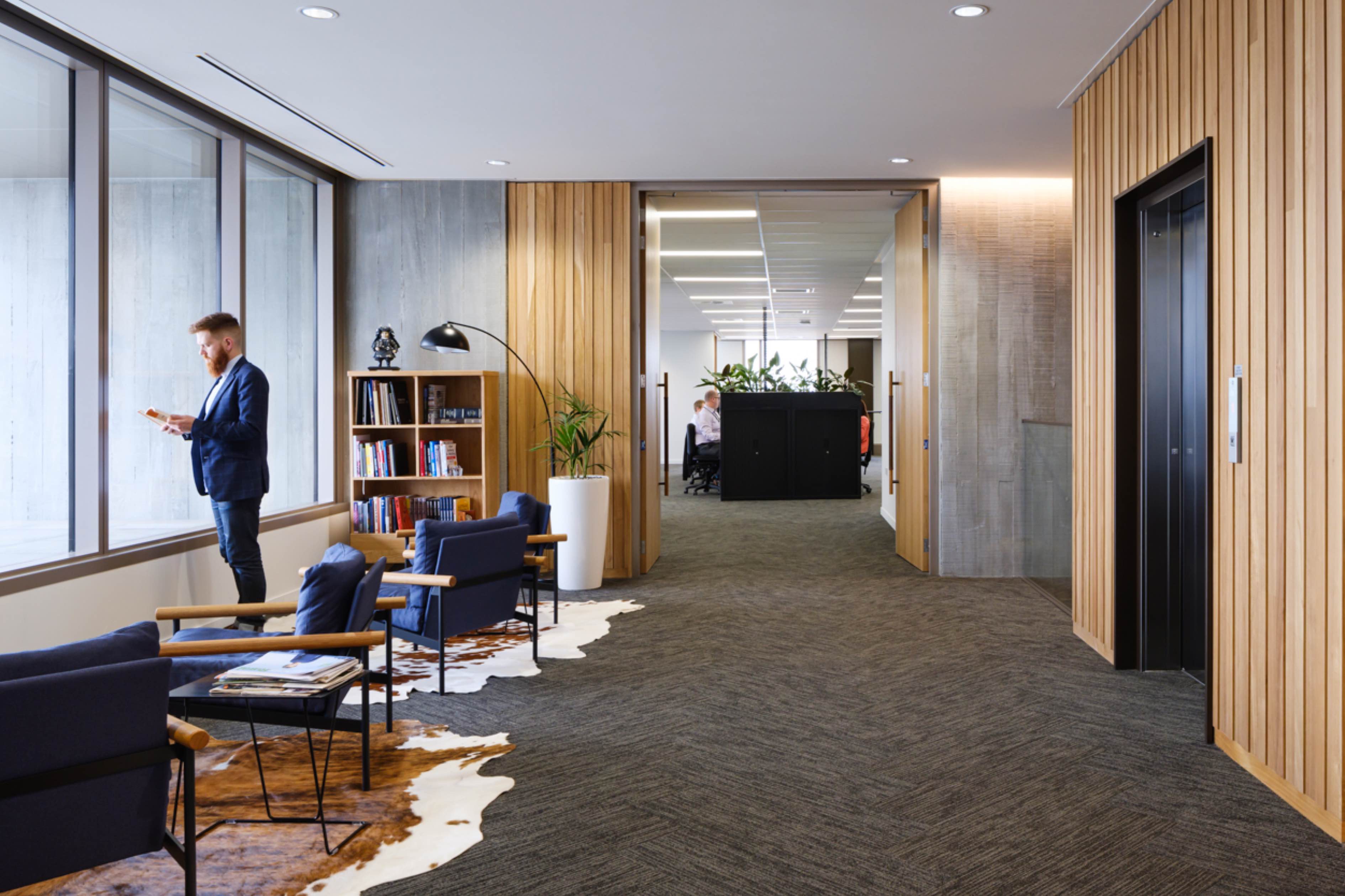 Suited man in waiting area with contemporary office space visible through open doorway
